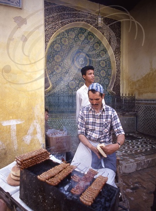 FÈS - la médina : vendeur de brochettes devant une fontaine en zelliges